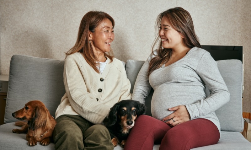 Pregnant woman sitting on a couch with another woman and two dogs