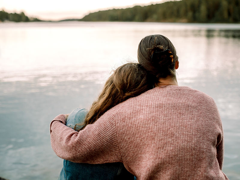 Mum hugging daughter while looking at lake