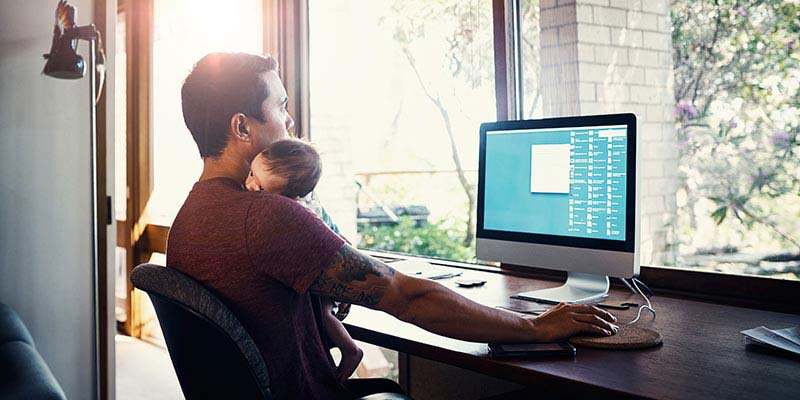 A dad cuddling his newborn while working A dad cuddling his newborn while working